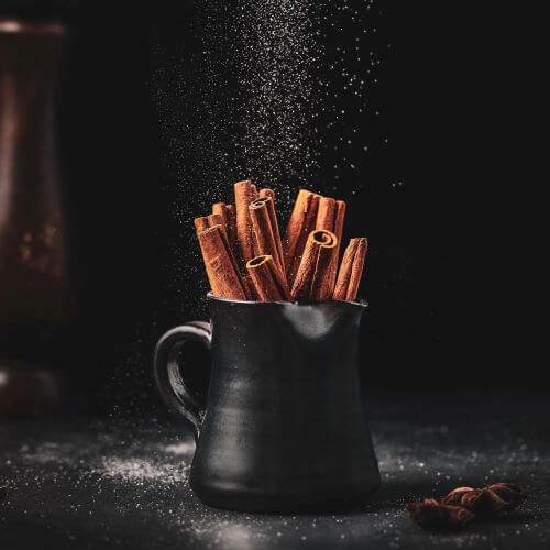 cinnamon sticks inside a black jar being sprinkled with sugar